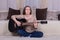 A young woman plays a black acoustic guitar on the carpet in the room