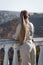 Young woman with ponytail stands leaning on balustrade and looks into distance, rear view