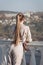 Young woman with ponytail stands leaning on balustrade and looks into distance, rear view