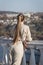 Young woman with ponytail stands leaning on balustrade and looks into distance, rear view