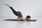 Young woman practices yoga asana Eka Pada Kaundiniasana 2 in the white room.