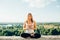 Young woman practices yoga outside. Calm smiling girl sits on parapet in lotus position with close eyes. Her fingers