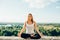 Young woman practices yoga outside. Calm smiling girl sitting on parapet in lotus position with closed eyes. Her hands