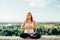 Young woman practices yoga outside. Calm smiling girl sitting on parapet in lotus position . Her hands at chest level