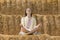 Young woman practices yoga sitting on the hay. Meditation in outside. Girl on farm sits on haystack