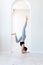 A young woman practices yoga and stands on her arms in the arch of a bright room. Young attractive yogi woman practicing yoga