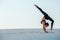 Young woman practicing inversion balancing yoga pose handstand on sand.