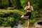 Young woman practicing yoga on a bridge near a decorative lake in the park. Summer day, yoga concept