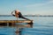 Young woman practicing yoga exercise at quiet wooden pier with city background. Sport and recreation in city rush