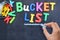 Young woman prepared for bucket list with metallic bucket and colorful plastic letters on blackboard