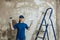 A young woman prepared to do repairs, smiling while standing on the background of a painted wall,