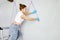 Young woman preparing wall for painting standing on ladder applying masking tape on wall. Diy project