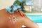 Young woman protecting her skin with sun lotion at the swimming pool, back view of an unrecognisable person