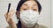 Young woman in protective surgical mask doing eye makeup looking at camera. Be beautiful during quarantine