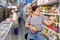 Young woman purchaser choosing tinned fish in big supermarket