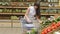 Young woman pushing cart along the grocery aisles in the supermarket. Girl choosing fresh vegetables in grocery and