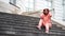 Young woman puts hood on head, sitting on stairs of manor. Adult female warms head in cool weather, sitting on steps of