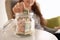 Young woman putting dollar banknote into glass jar indoors, closeup. Money savings concept