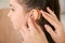 Young woman putting hearing aid in daughter`s ear, closeup