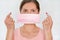 Young woman putting pink cotton home made virus mouth face mask on, holding it in front of her, portrait on white background, can