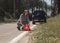 Young woman putting red triangle caution sign on road near broken car on roadside