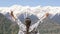 A young woman raises her arms up in front of a high snow-capped mountain