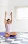 Young woman raising arms in lotus position, preparation for yoga practice in minimalist bright ambience