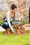 Young woman raking dry leaves autumn backyard