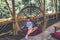 Young woman in the rattan lounge hanging chair with pillow at the balcony with green nature tropical background.