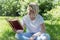 Young woman reading a book in a park on a sunny summer day. Blonde in a white T-shirt and jeans. Leisure and hobbies