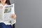 Young woman reading newspaper against grey background