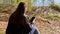 Young Woman Reading Text Message in a Smartphone, Sitting on Fallen Dry Leaves