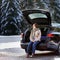 Young woman ready to go on vacations and relaxing in the opened trunk of a car before a road trip