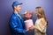 Young woman receiving beautiful flowers and gift from delivery man on color background