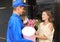 Young woman receiving beautiful flowers and gift from delivery man outdoors