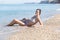 Young woman reclines leaning on elbow on pebbles on beach