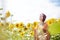 Young woman with red burgundy hair, wearing boho hippie clothes, standing in the middle of yellow sunflowers field, looking at sky