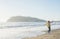 Young woman in red checkered shirt, jeans, white sneakers walking along beach and the stormy ocean on sunny winter day