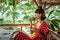 Young woman in red dress drinking a coffee in a tropical restaurant on Bali island. Travel, jungle, rainforest of Indonesia.