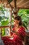 Young woman in red dress drinking a coffee in a tropical restaurant on Bali island. Travel, jungle, rainforest of Indonesia.