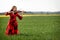 Young woman in red dress playing violin in green meadow - image