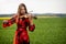 Young woman in red dress playing violin in green meadow - image