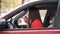 Young woman in a red dress in red car paints her lips red. Girl driver preening