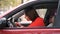 Young woman in a red dress in red car paints her nails red. Girl driver preening