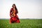 Young woman in red dress with violin in green meadow - image