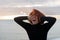 Young woman with red hair clutching her head and loudly screaming from heartache on the background of sea and sunset