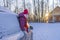 Young woman in a red hat peeking out of a snow-covered car on the background of a winter road and the setting sun