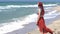 Young woman in a red skirt and blue top with red hair flying in the wind looks at the stormy sea