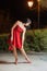 Young woman in red sleeveless dress walking in night park