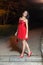 Young woman in red sleeveless dress walking in night park